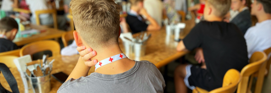 Jugendlicher, der an einem Tisch sitzt, umgeben von anderen Jugendlichen.